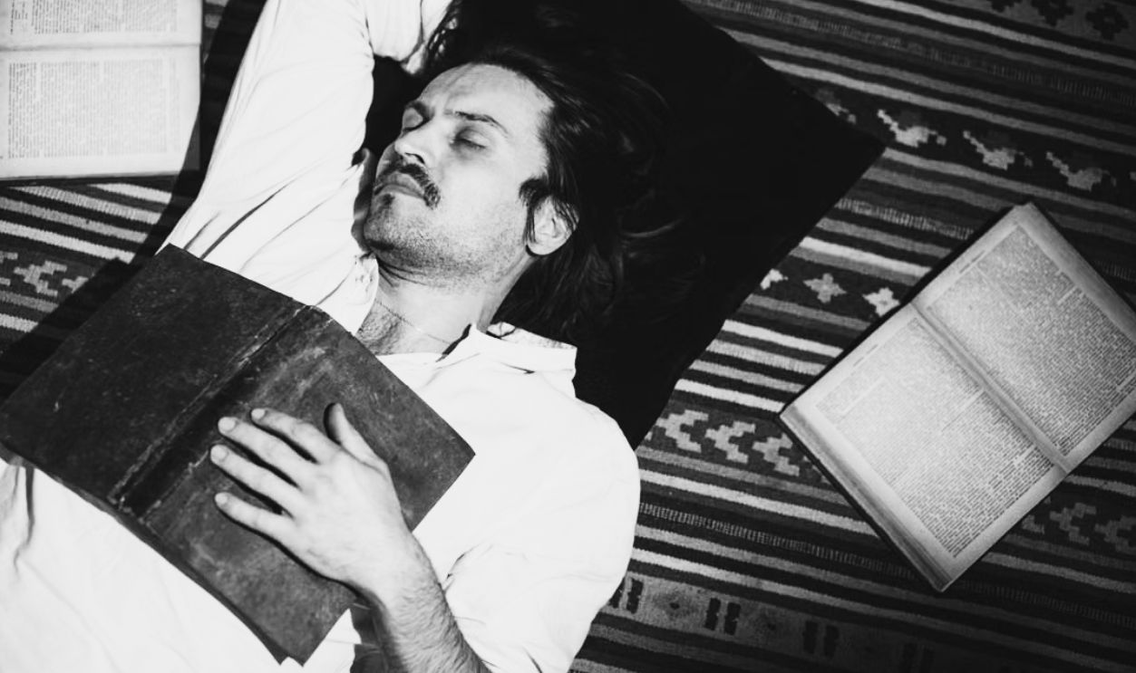 Adult man peacefully sleeping on striped carpet surrounded by open books indoors