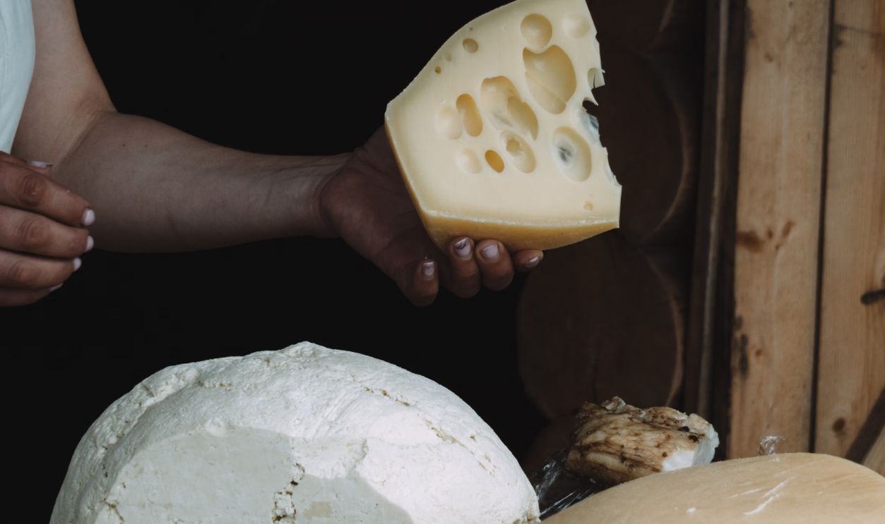 Close-up of various cheeses displayed on a rustic wooden table with a person holding a slice