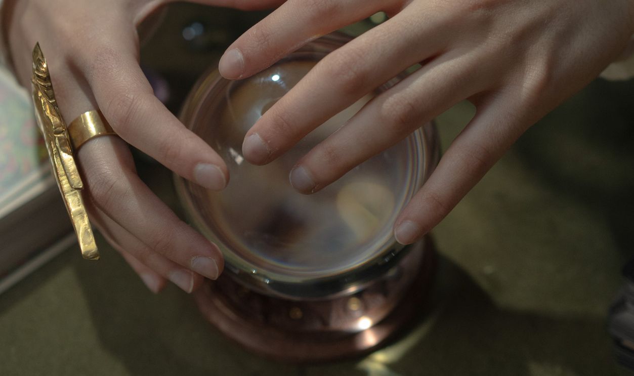 Hands of a fortune teller hovering over a crystal ball, hinting at esoteric mysteries
