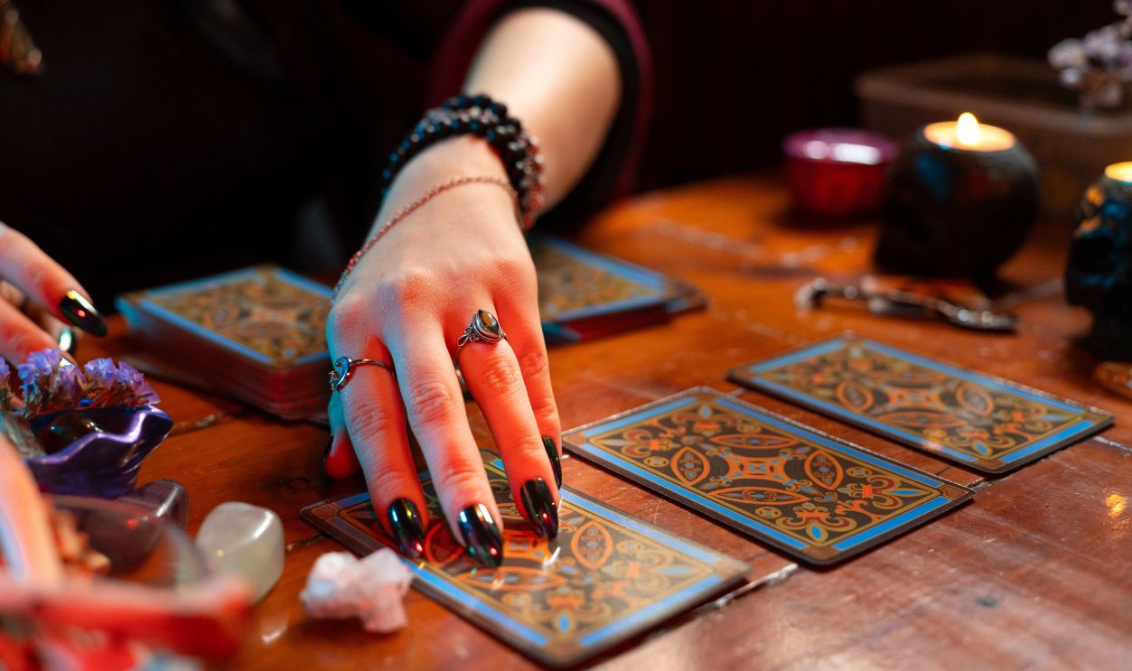 Fortune teller reading tarot cards on a wooden table with candles and crystals, predicting the future with esoteric and mystical arts