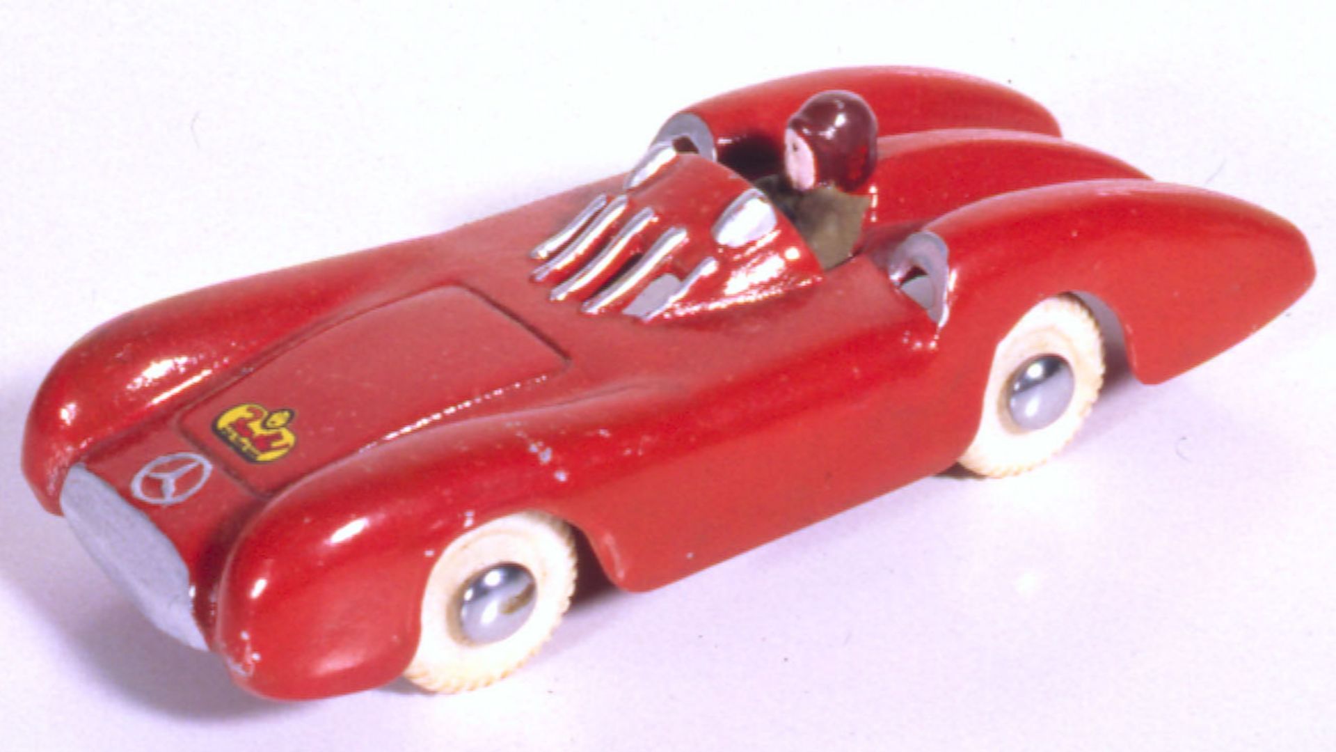 Mercedes-Benz racer cast aluminium orange car with pink face driver, red had, brown clothing, white plastic wheels, tin axles.