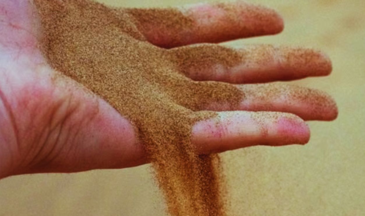 Close-up of a hand letting sand fall naturally in a desert, symbolizing time and nature