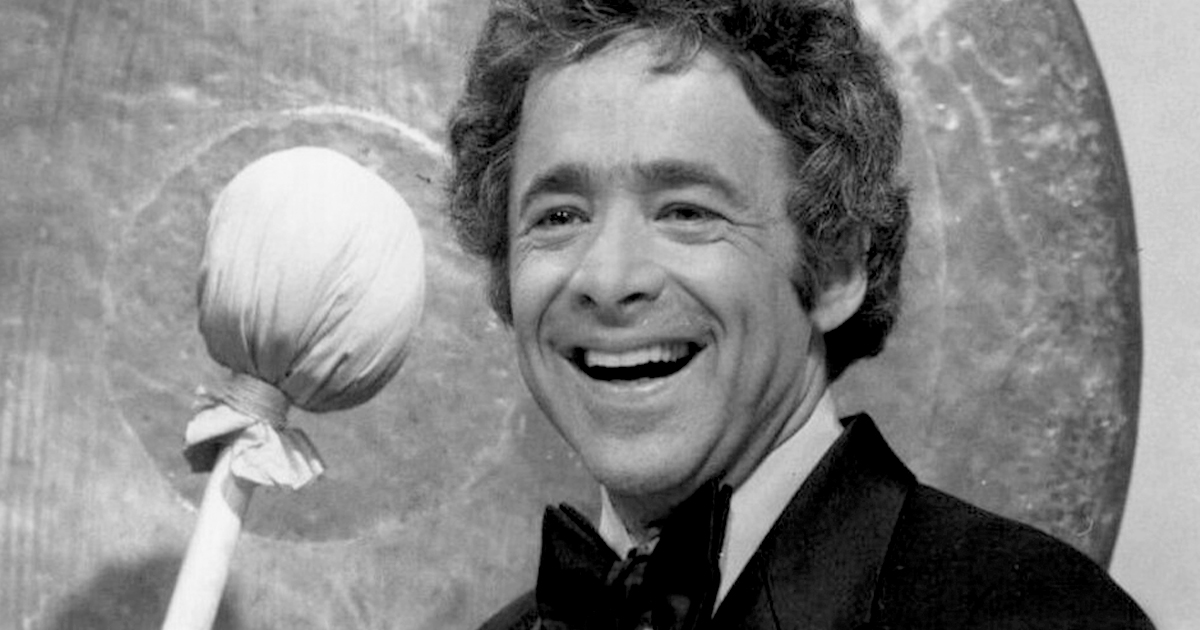 Black and white photo of Chuck Barris in a suit holding a gong