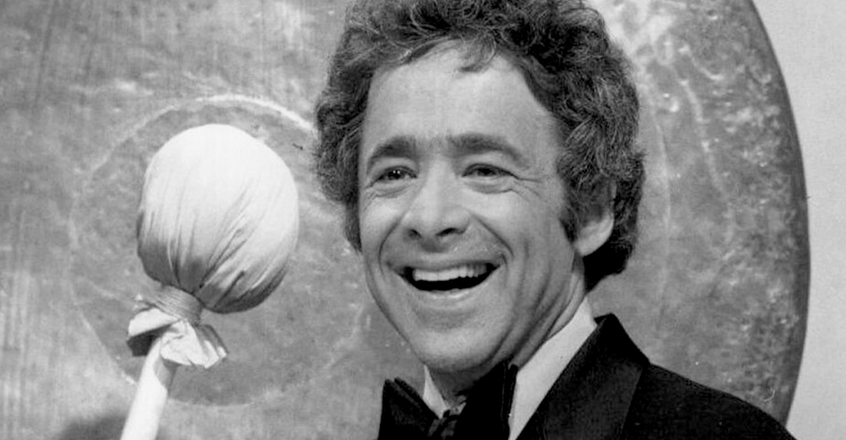Black and white photo of Chuck Barris in a suit holding a gong