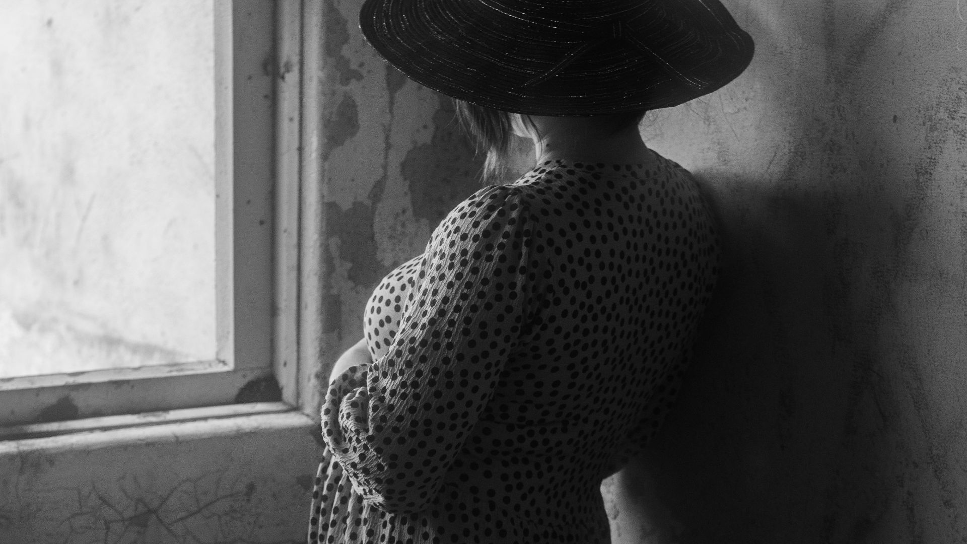a woman in a dress and hat leaning against a wall