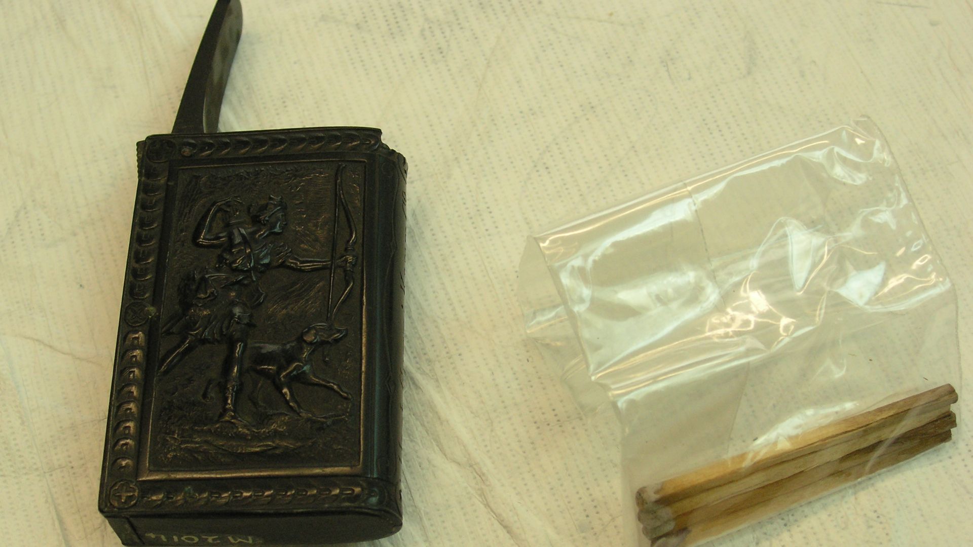 Box, match, bakelite, black press-mounted match box with two panels depicting Diana the huntress and her quarry.Flip toped lid - Inscribed Harb.Gummi-Kamm Co.