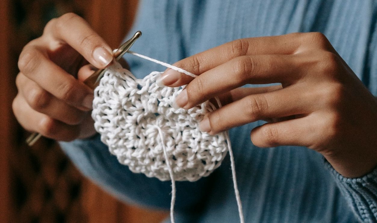 A person knitting a blue sweater by hand in a cozy indoor setting