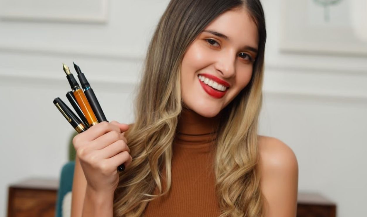 Portrait of a cheerful woman holding fountain pens, showcasing creativity indoors