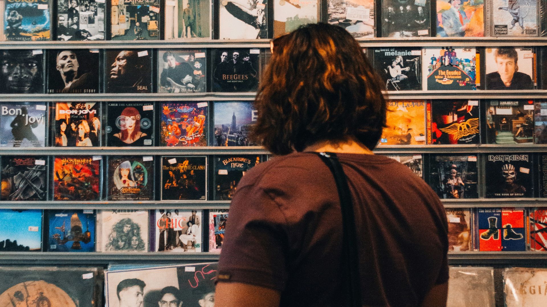 A person with wavy hair browsing a wall of vinyl record covers