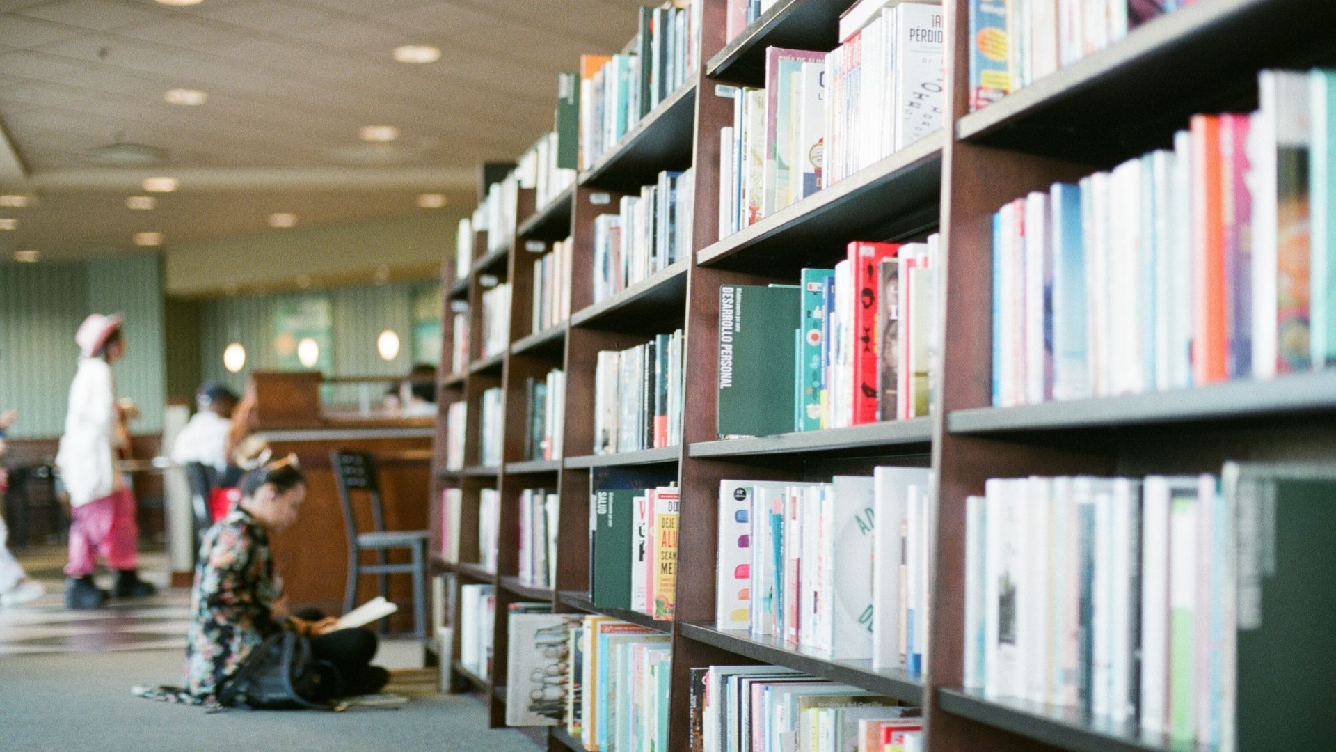 woman reading book in front of bookshelves
