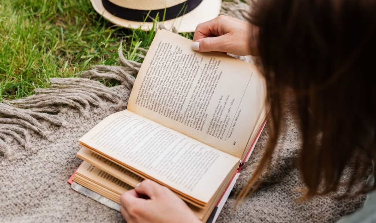 A woman enjoying a peaceful reading session on a grassy area with a hat nearby