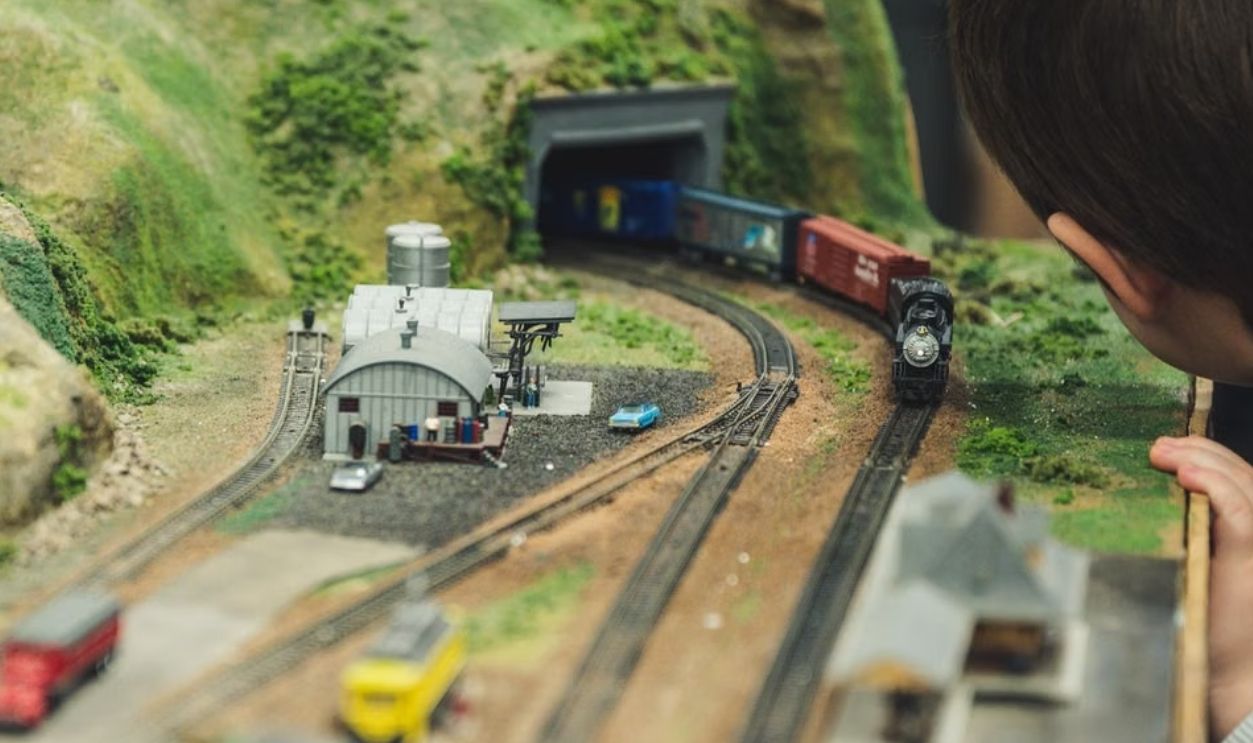 A child plays with a model train set indoors, showcasing curiosity and engagement