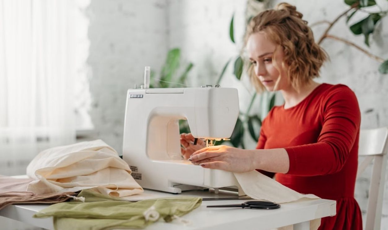 A woman in a red dress using a sewing machine at home, creating a handmade garment