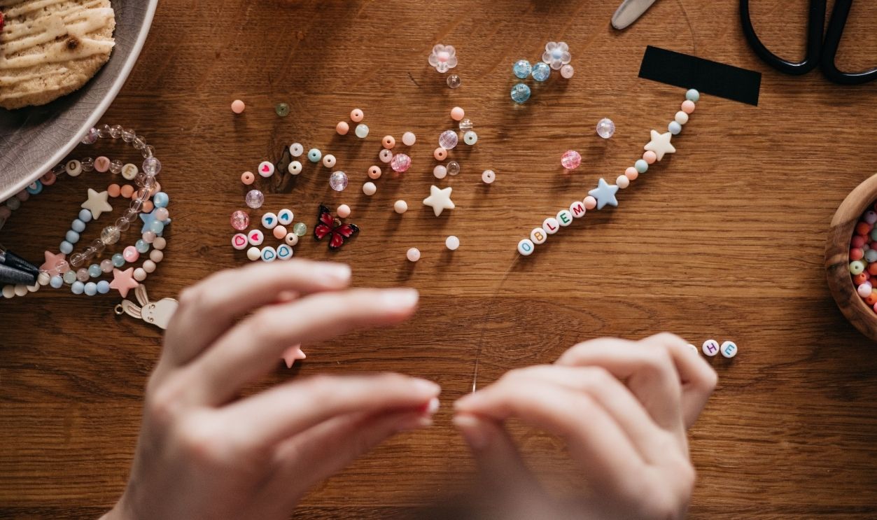 Hands crafting personalized jewelry with beads at a well-organized wooden table