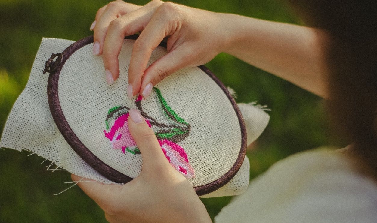 A woman embroidery flowers on fabric in sunlight, showcasing a delicate handmade touch