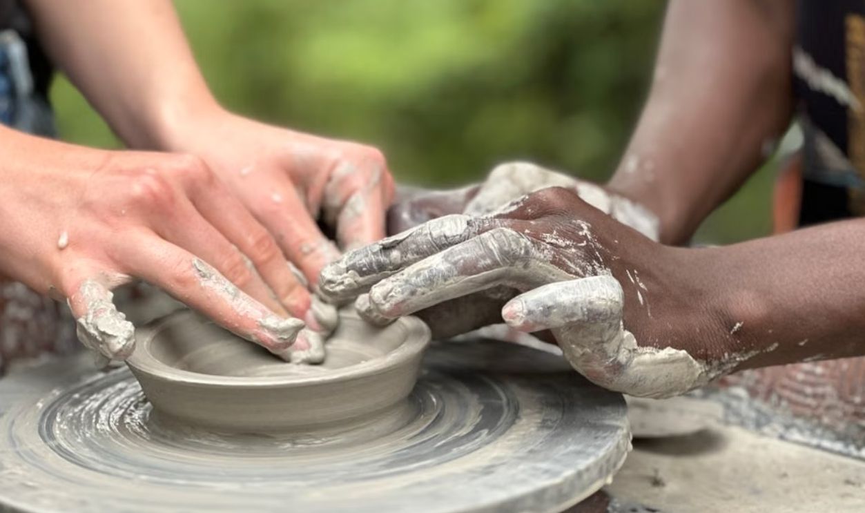 Two people crafting pottery together, hands covered in clay, symbolizing teamwork