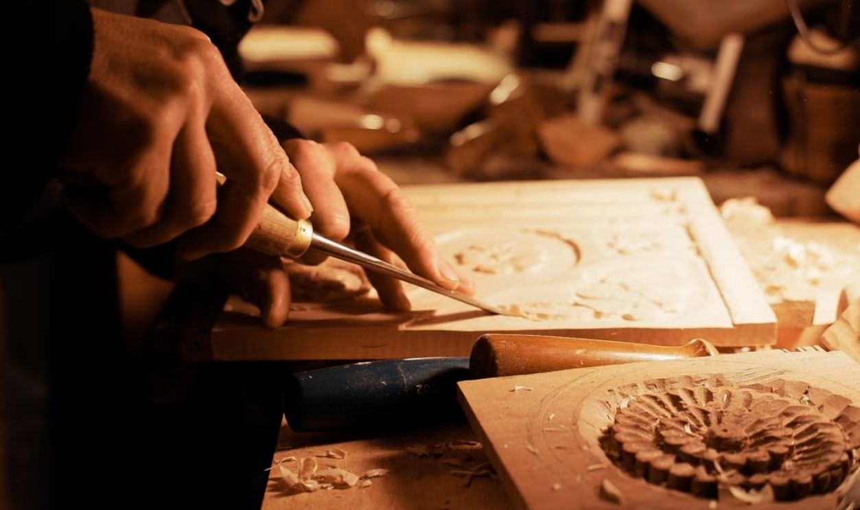 Craftsman skillfully carves intricate designs into wood under warm lighting