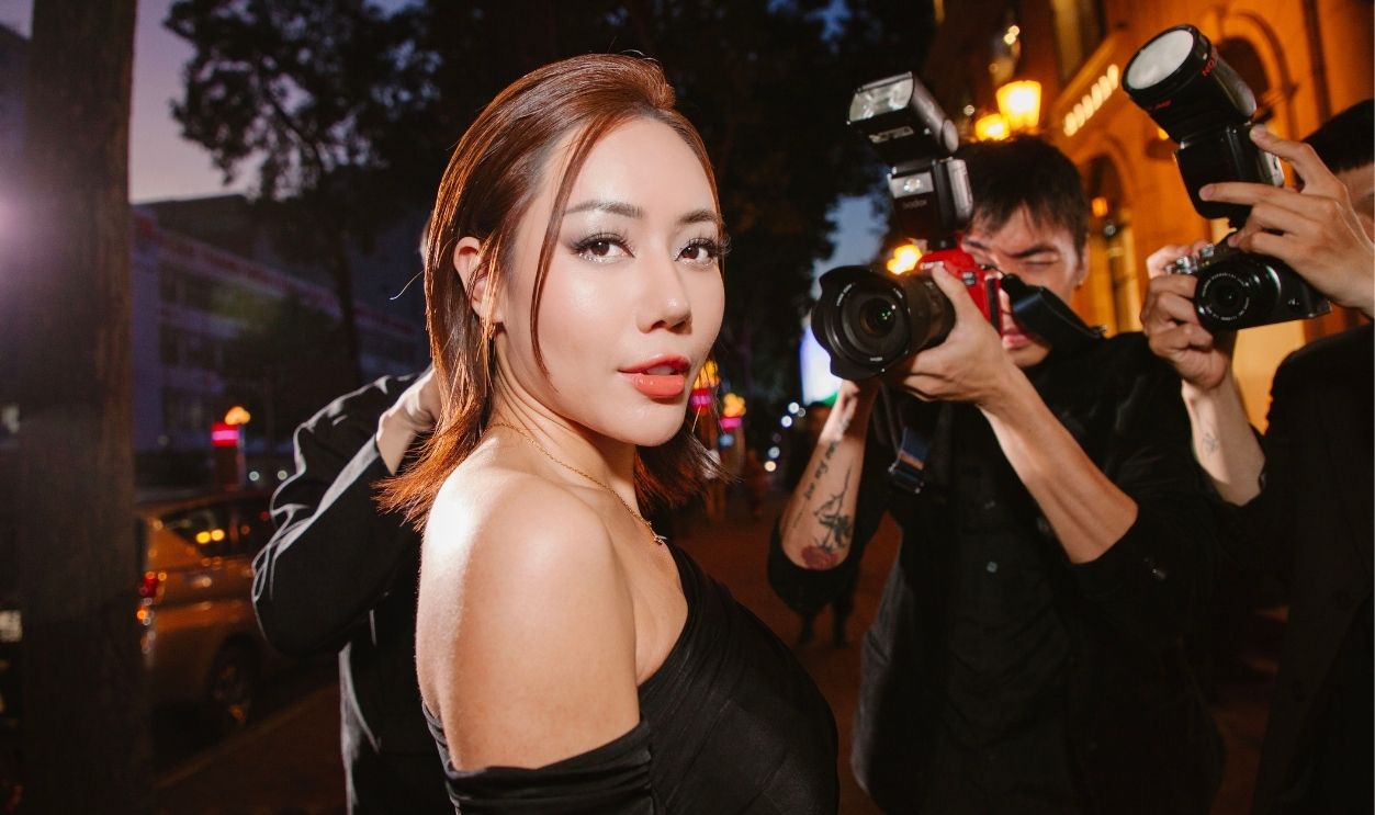 A glamorous woman in black poses confidently for photographers at a night event