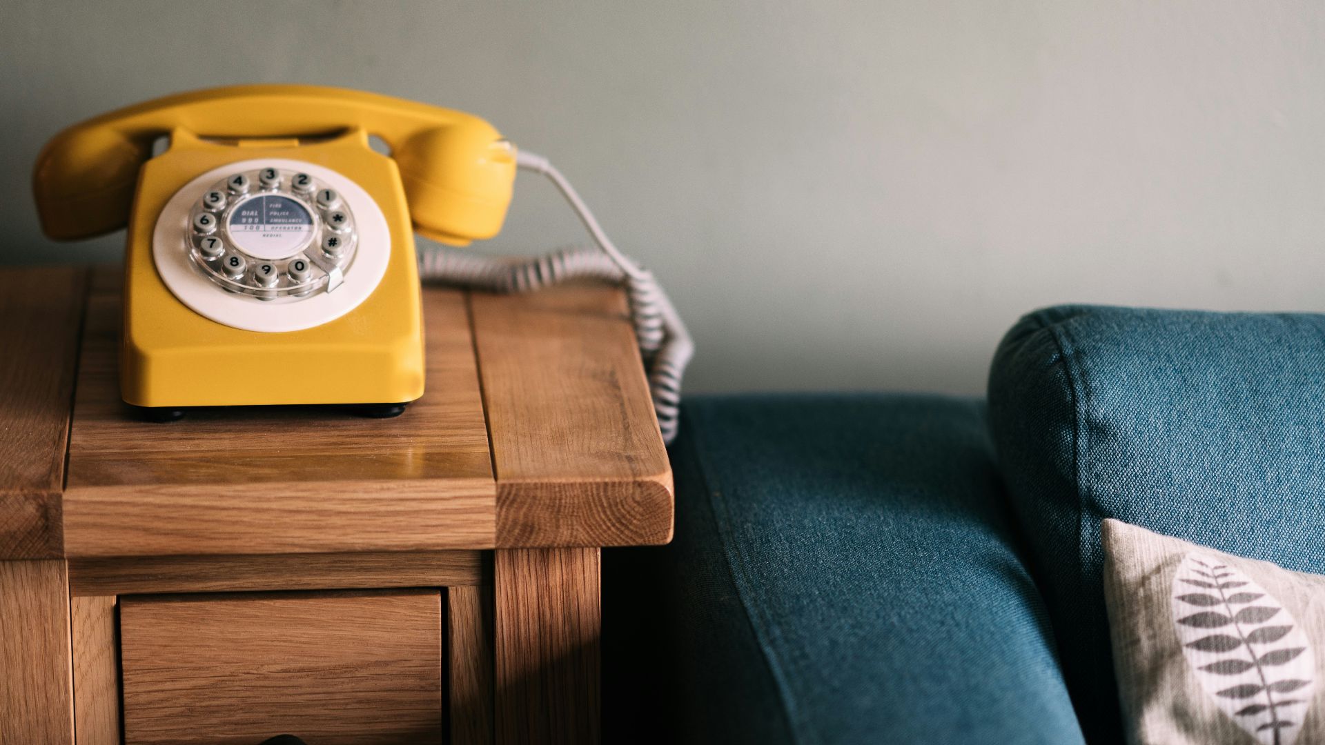 photo of yellow rotary telephone near blue sofa