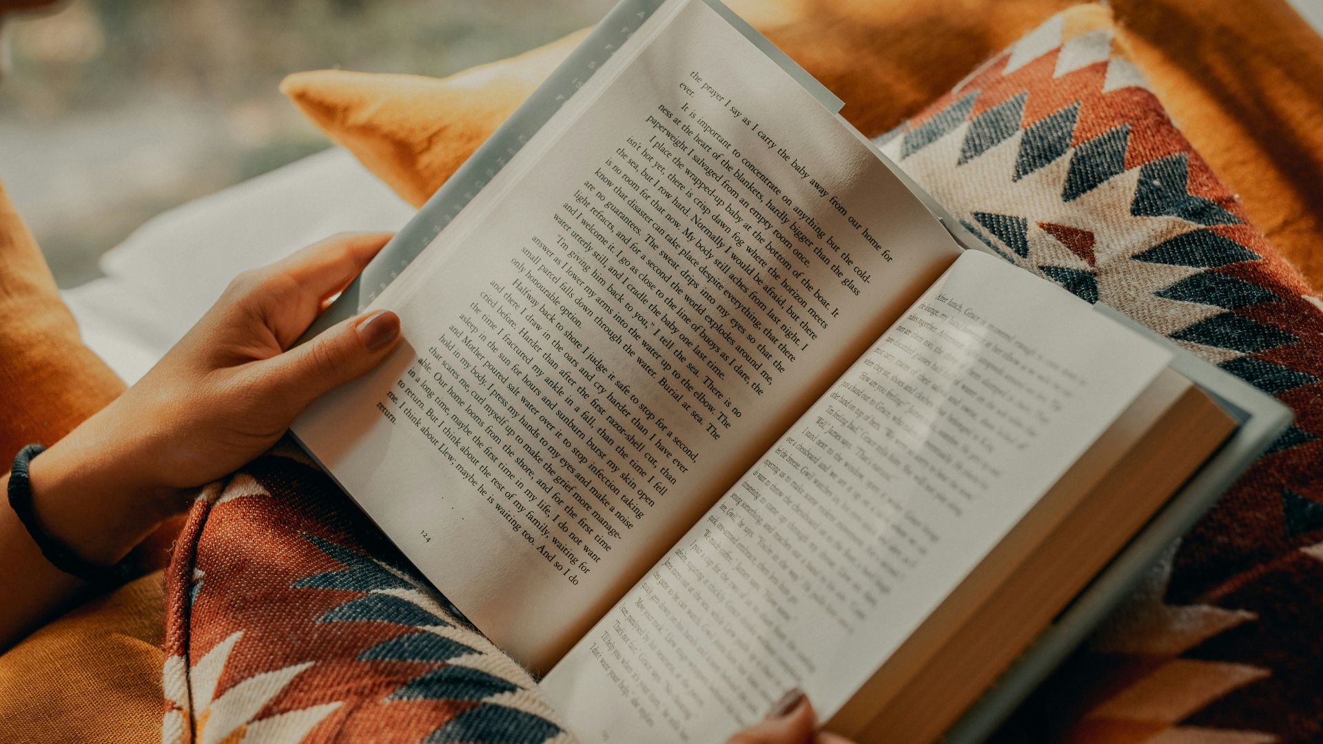 person reading book on brown and beige textile