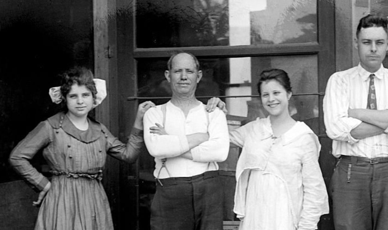 Two sisters and the a brother pose with their father outside his general store at the end of World War I. 