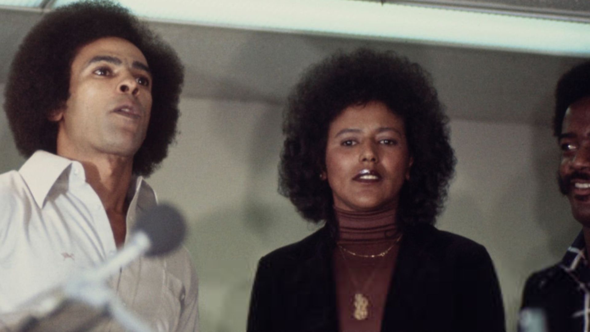 Black Panther Party co-founder Huey Newton (centre, 1942 - 1989) speaking to a crowd of circa 500 Black Panthers on arrival at San Francisco International Airport, California, July 5th 1977. He is with his wife Gwen (left) and Black Panther chairwoman Ela