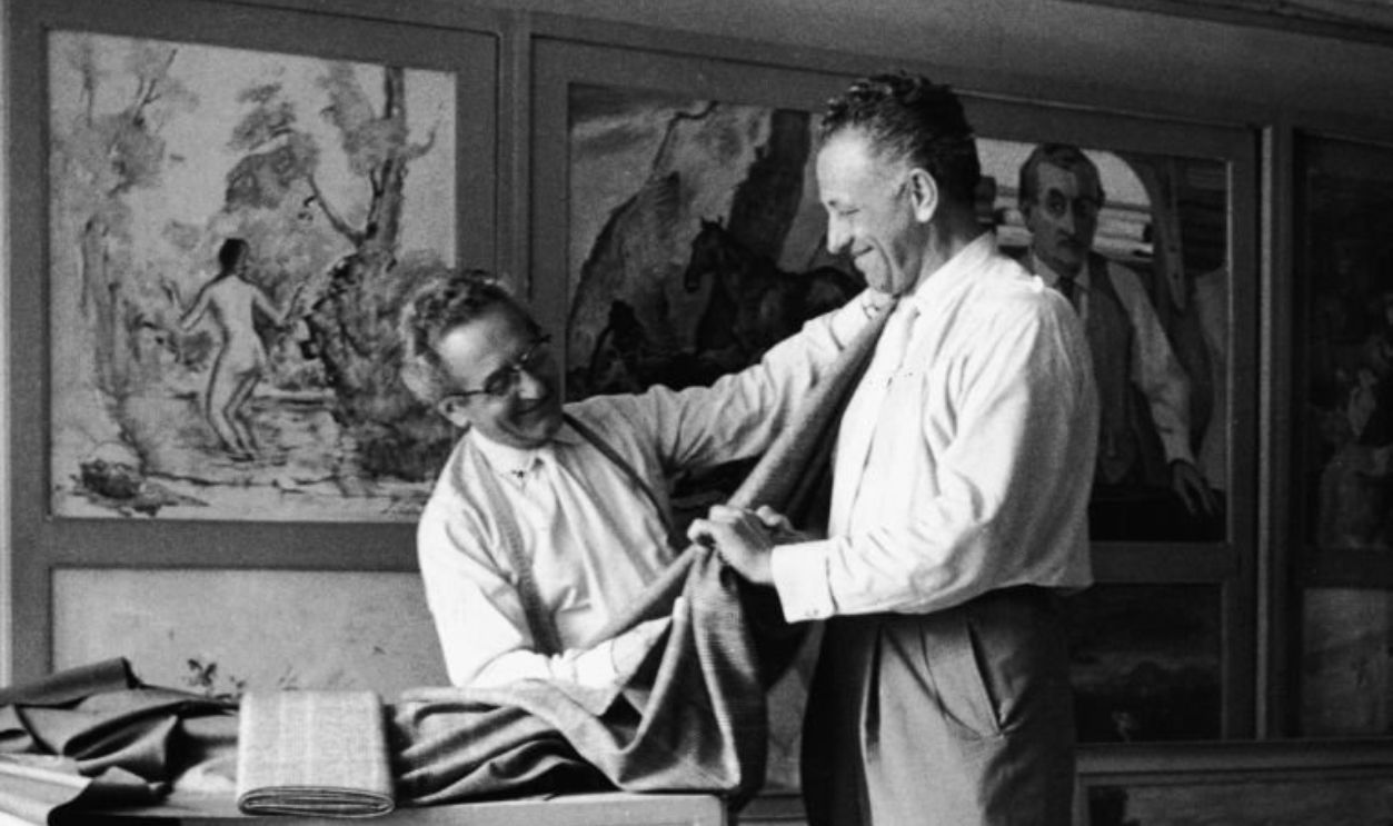 American film director Nicholas Ray (1911 - 1979) (right) is custom fitted by a tailor while in Venice for the Italian premiere of his film 'Amere Victoire' (released in the US as 'Bitter Victory') at the Venice Film Festival, September 1957. The tailor's shop is decorated with many paintings. 