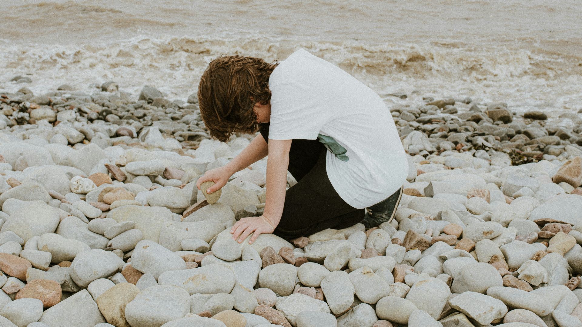 a person kneeling down on a rocky beach