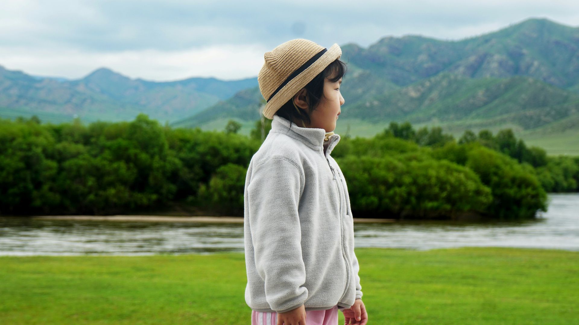 Young child in a hat by a river and mountains