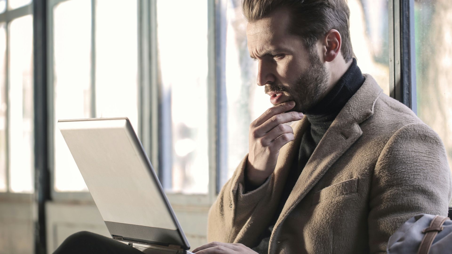 man holding his chin facing laptop computer