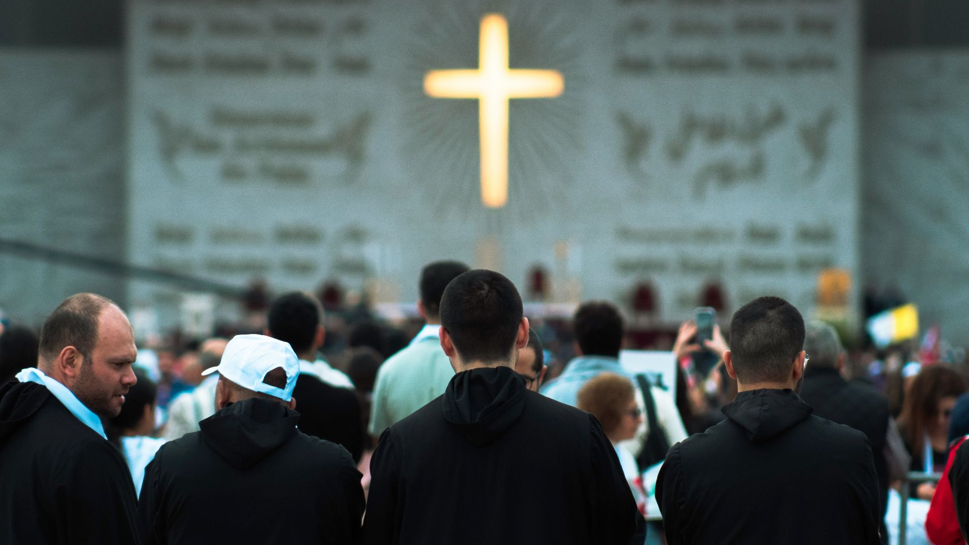People gathered before a large illuminated cross