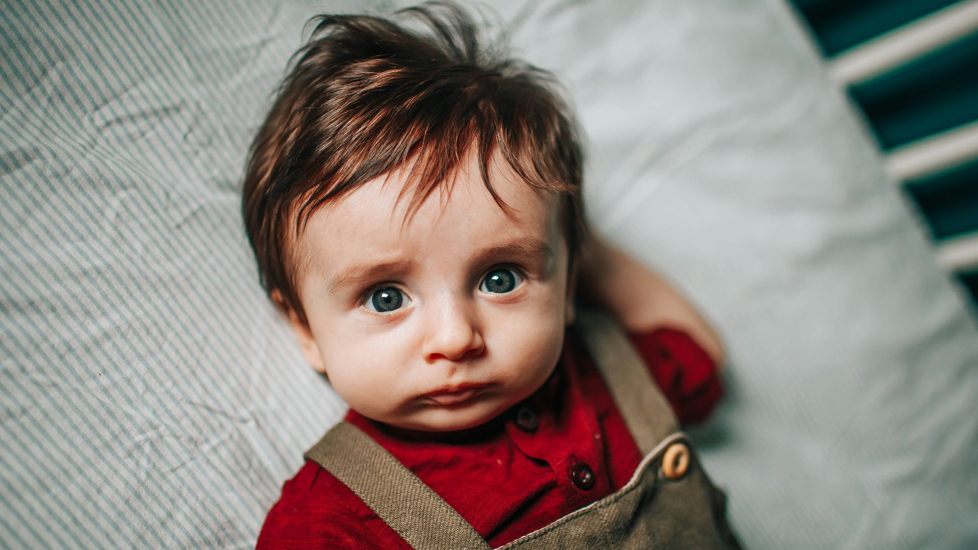 boy in red and brown jacket lying on white textile
