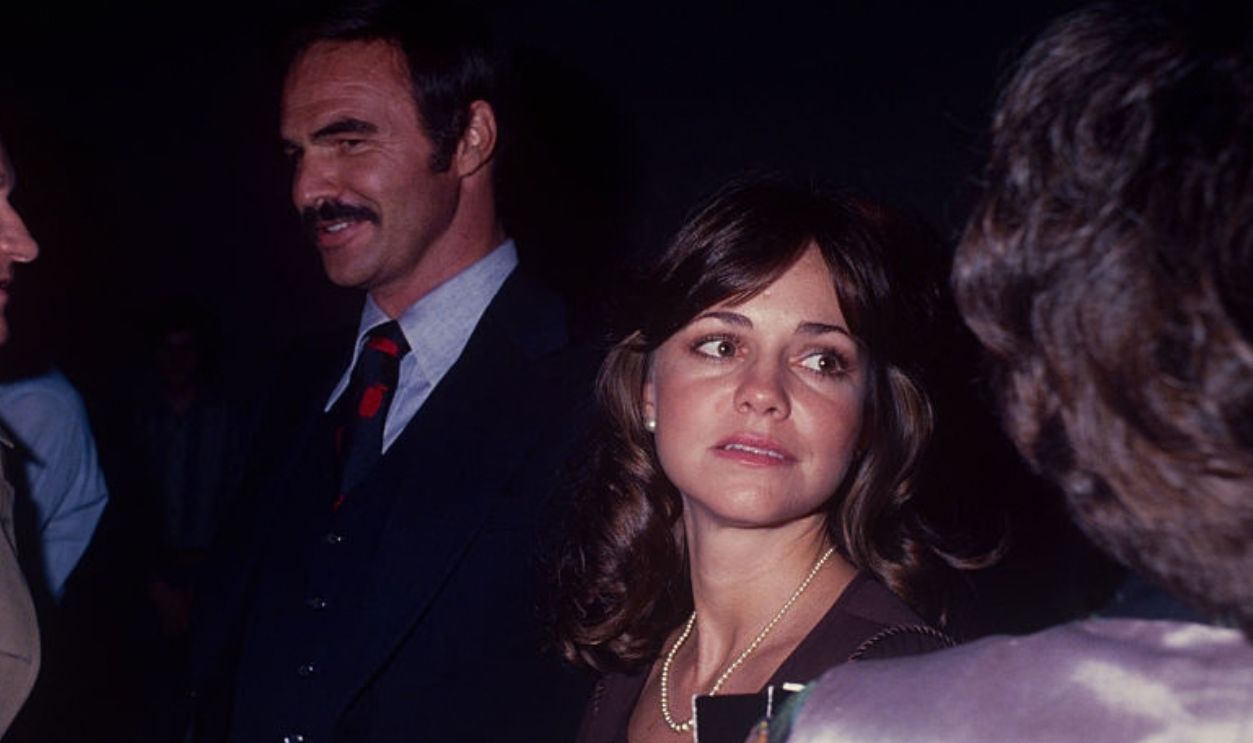 Sally Field with Burt Reynolds talking with friends; circa 1970; New York.