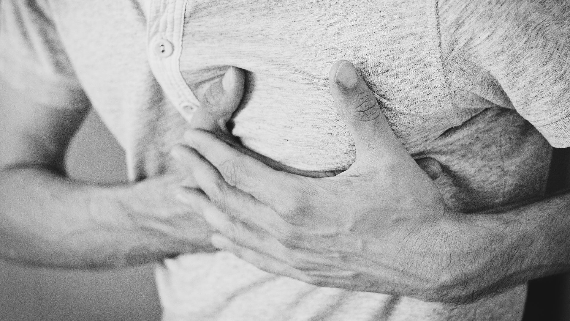 Black and white photo of a man clutching his chest, indicating discomfort or pain.