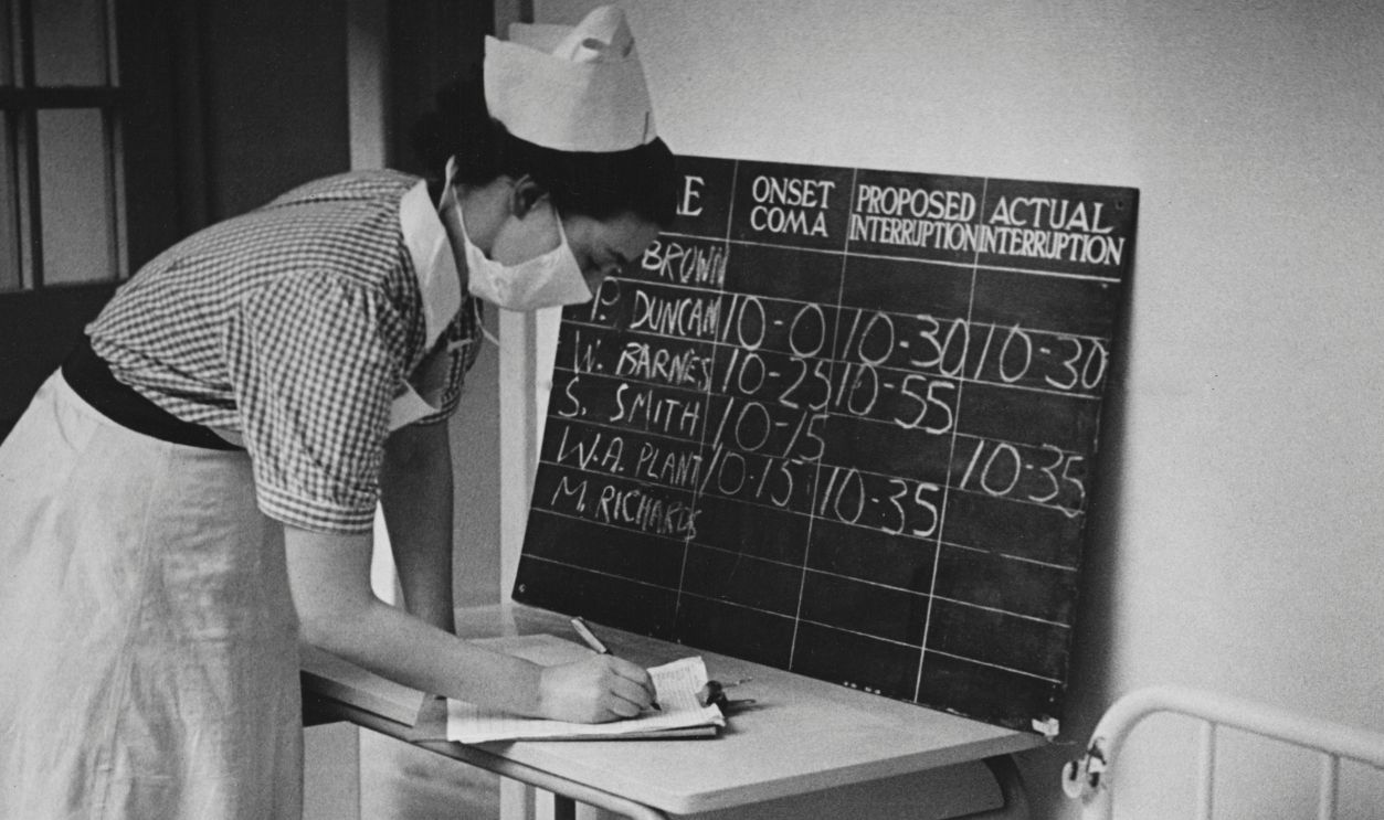 A nurse checks on a psychiatric patient who lies in a state of insulin-induced coma. To break the coma, a dose of sugar is administered.