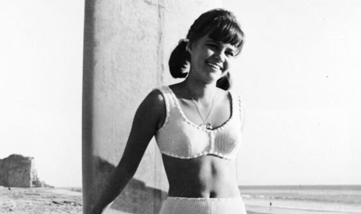 Promotional portrait of American actor Sally Field from the television series, 'Gidget,' posing in a swimsuit with a surfboard on the beach, circa 1965.