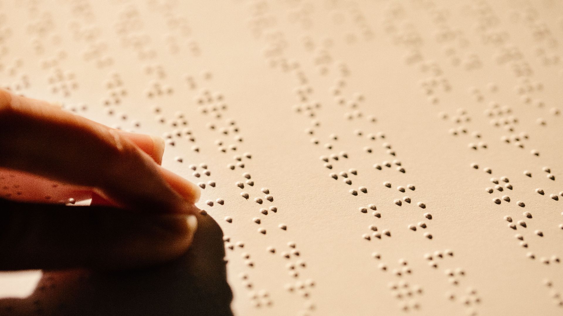 A close-up image of a hand touching embossed Braille text on a paper sheet, highlighting tactile reading.