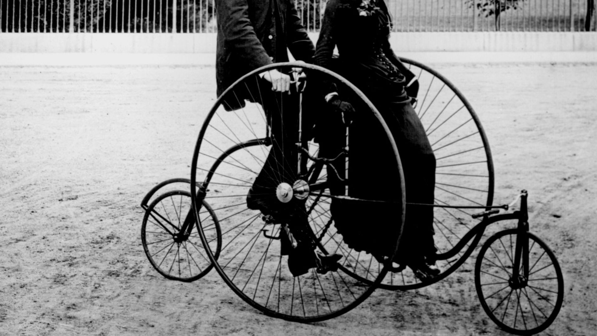 Smartly dressed couple seated on an 1886-model quadracycle for two. The South Portico of the White House, Washington, D.C., in the background.
