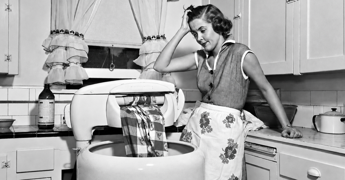 1950s frustrated housewife with jammed wringer on clothes washing machine in kitchen