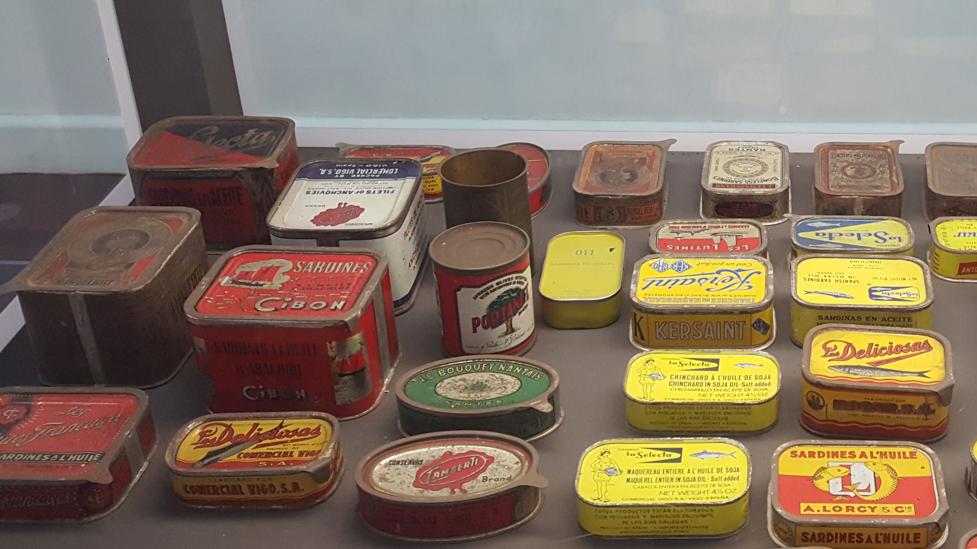 Vitrina cun conxunto de latas de conservas antigas en diferentes idiomas, pódense ver latas de sardiñas mais tamén de polbo á mariñeira.