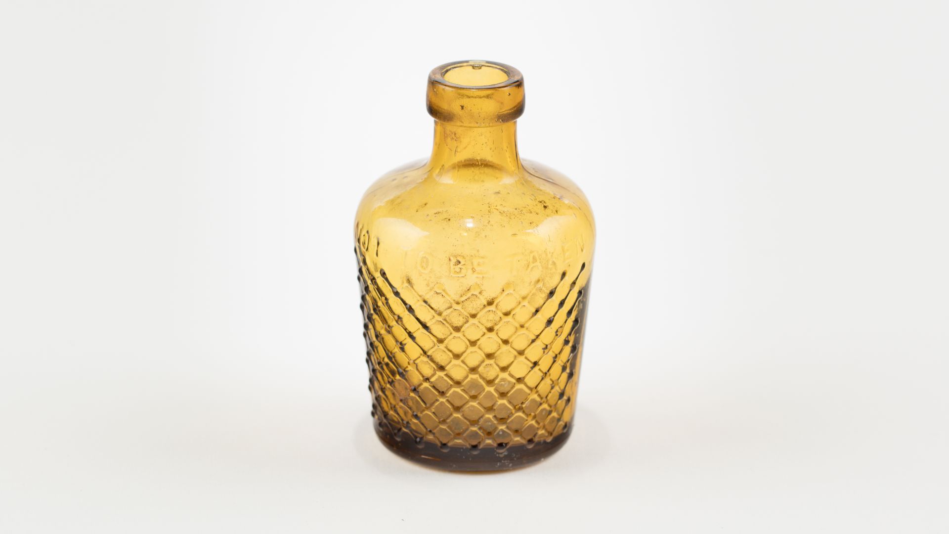 Poison bottle amber coloured glass; cork closure top, no cork present; thick lip connecting to short neck, exaggerated broad shoulders; cylindrical body, slight taper towards base; directly below shoulders, on body, raised embossed text reads- POISON; rev