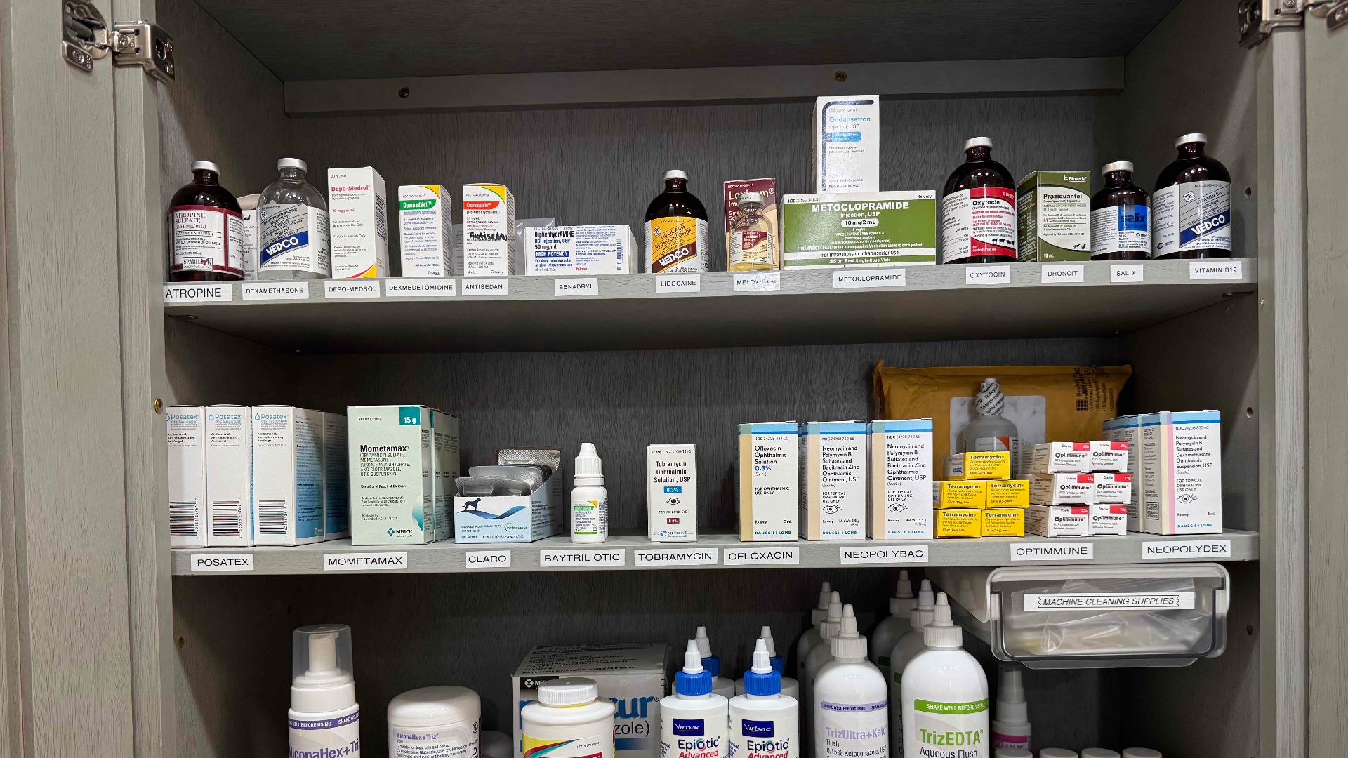 An open cabinet contains medicine bottles, cartons, and other supplies on labeled shelves at a veterinary clinic in Newark, New Jersey.