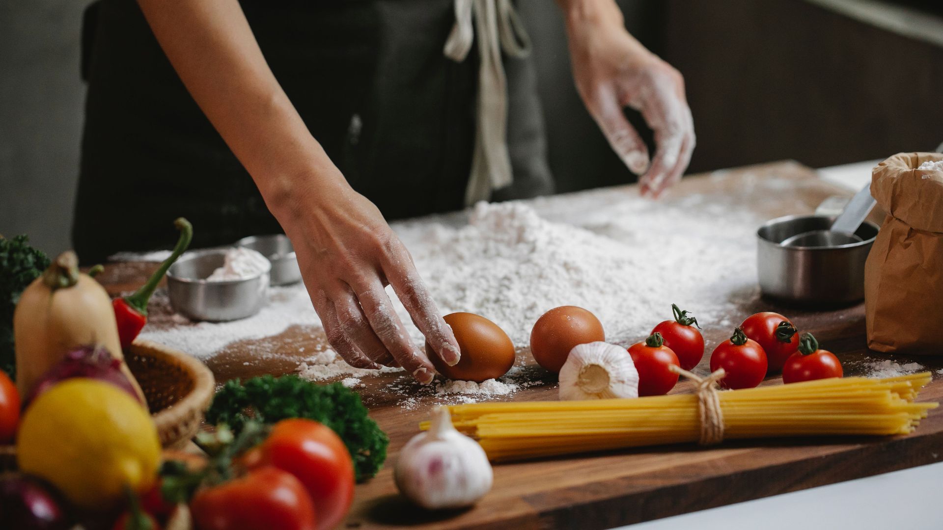 High angle of crop anonymous chef preparing meal consisting of eggs garlic cherry tomatoes and spaghetti