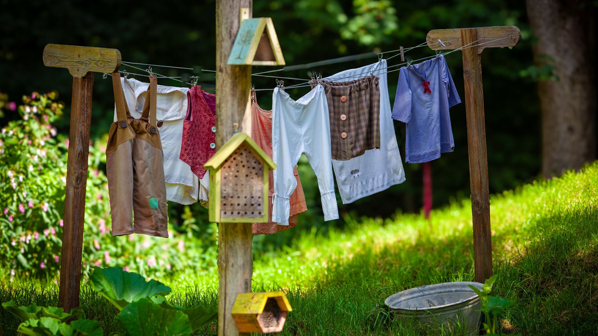 Children's clothes drying on a rustic clothesline in a garden setting.