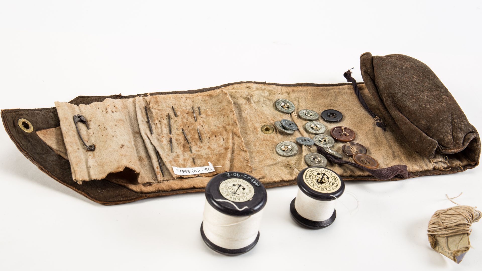 Military sewing kit or housewife (hussif), 1NZEF, WW1 sewing kit of brown suede with three reels of cotton, buttons, thread and needles comprises .1 holder .2-.4 cotton reels .5 seven metal buttons .6 three plastic buttons .7 wad of thread and needles