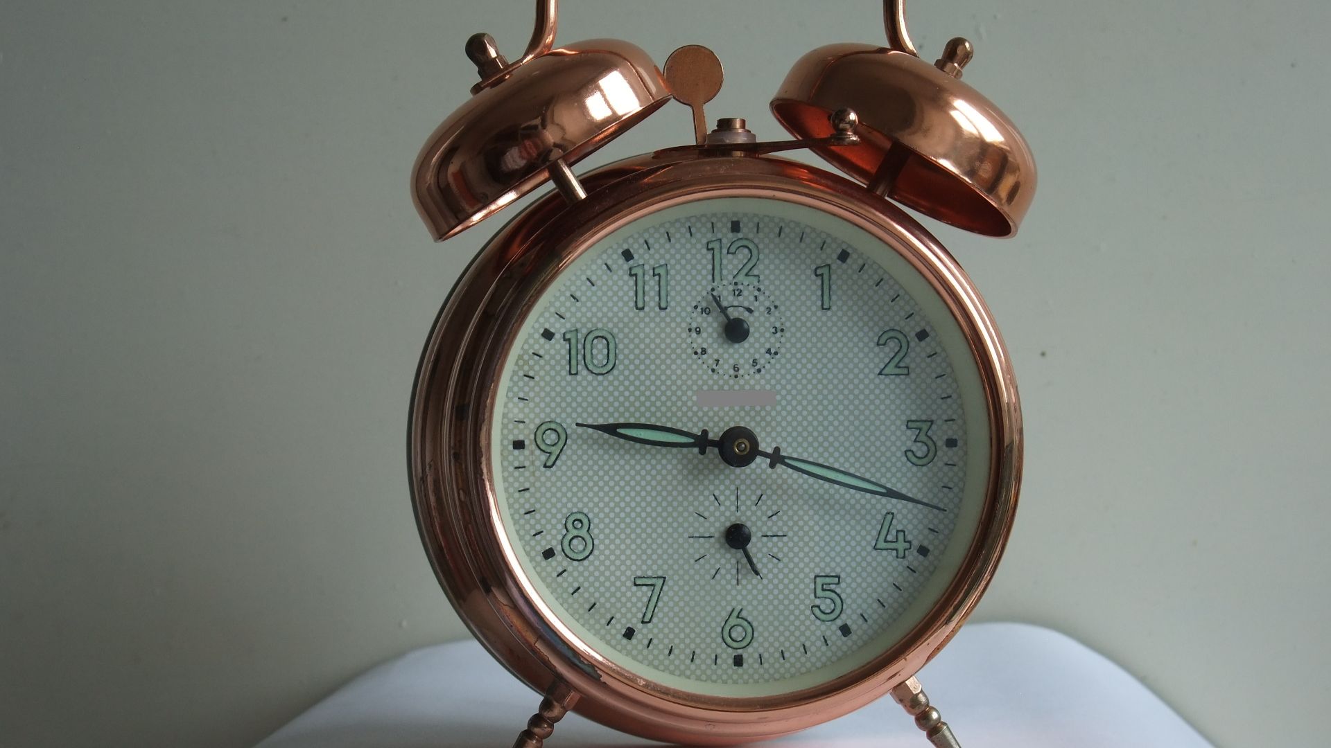 Copper-plated mechanical alarm clock of unknown origins. Manufacturer's name has been blanked out and no country of origin is visible.