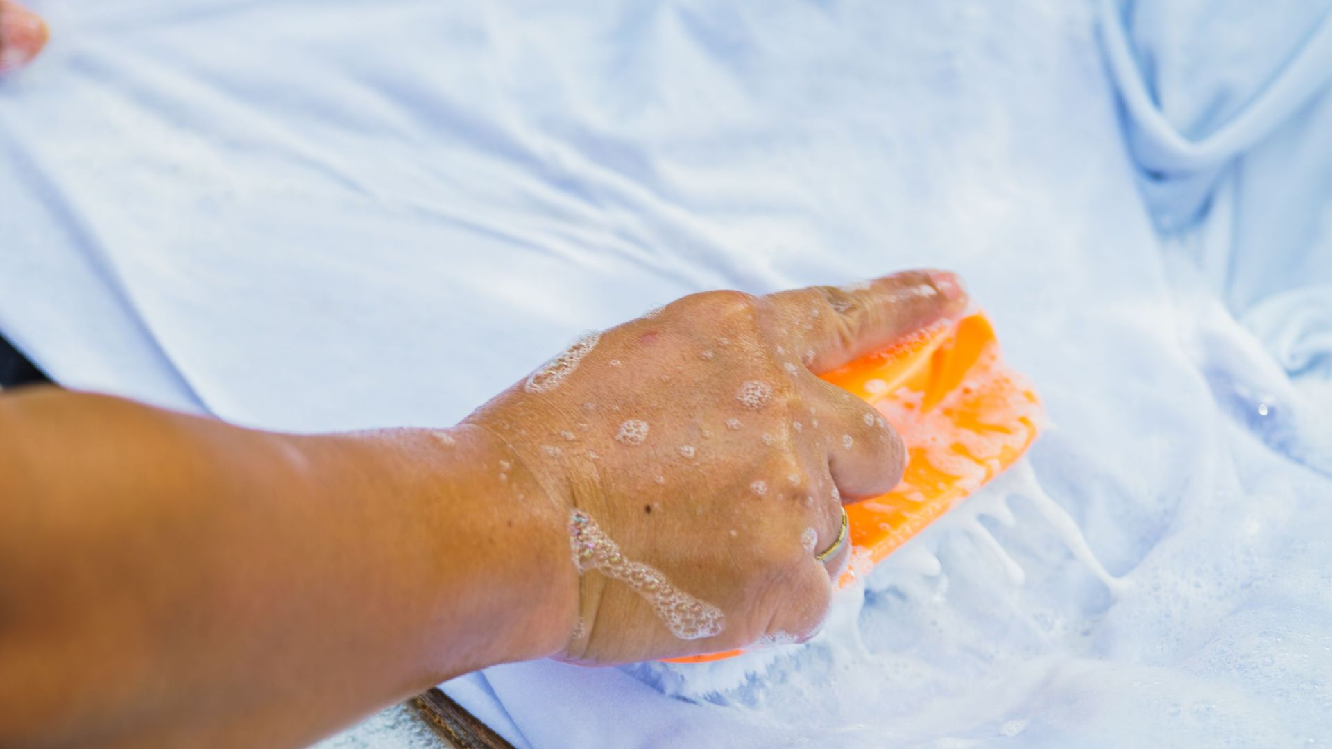 A person handwashing a white shirt with soap in a basin outdoors, showing manual laundry technique.