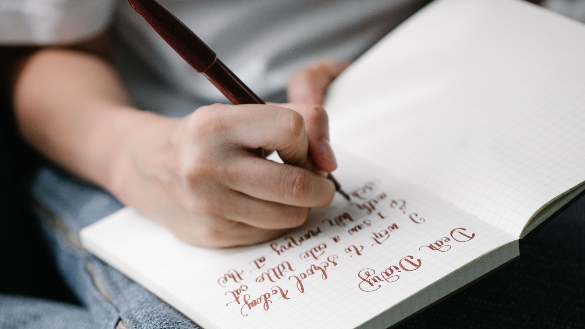 Person writing in a notebook with elegant handwritten calligraphy.