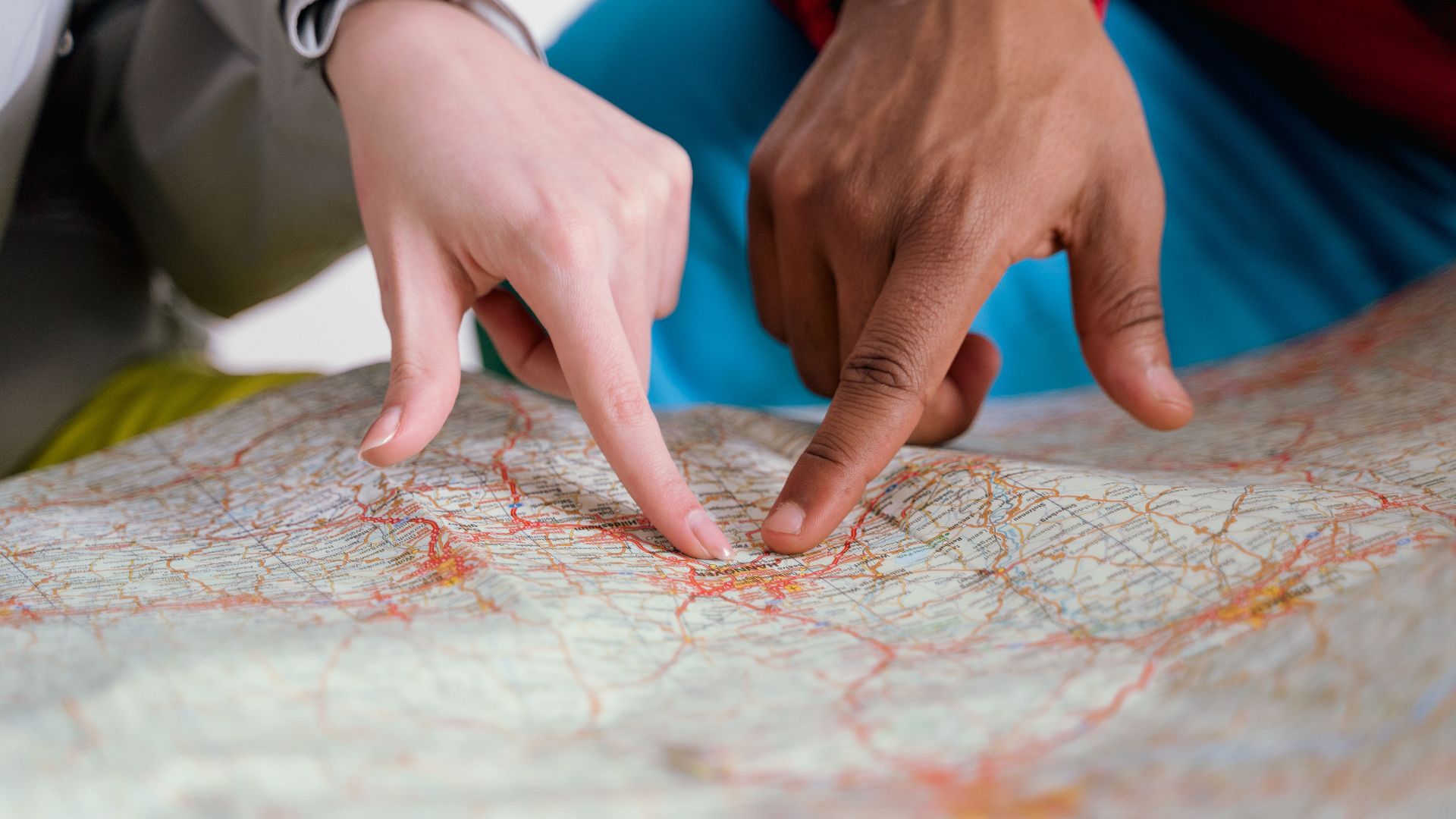 Close-up of diverse hands pointing at a paper map, symbolizing travel planning and navigation.
