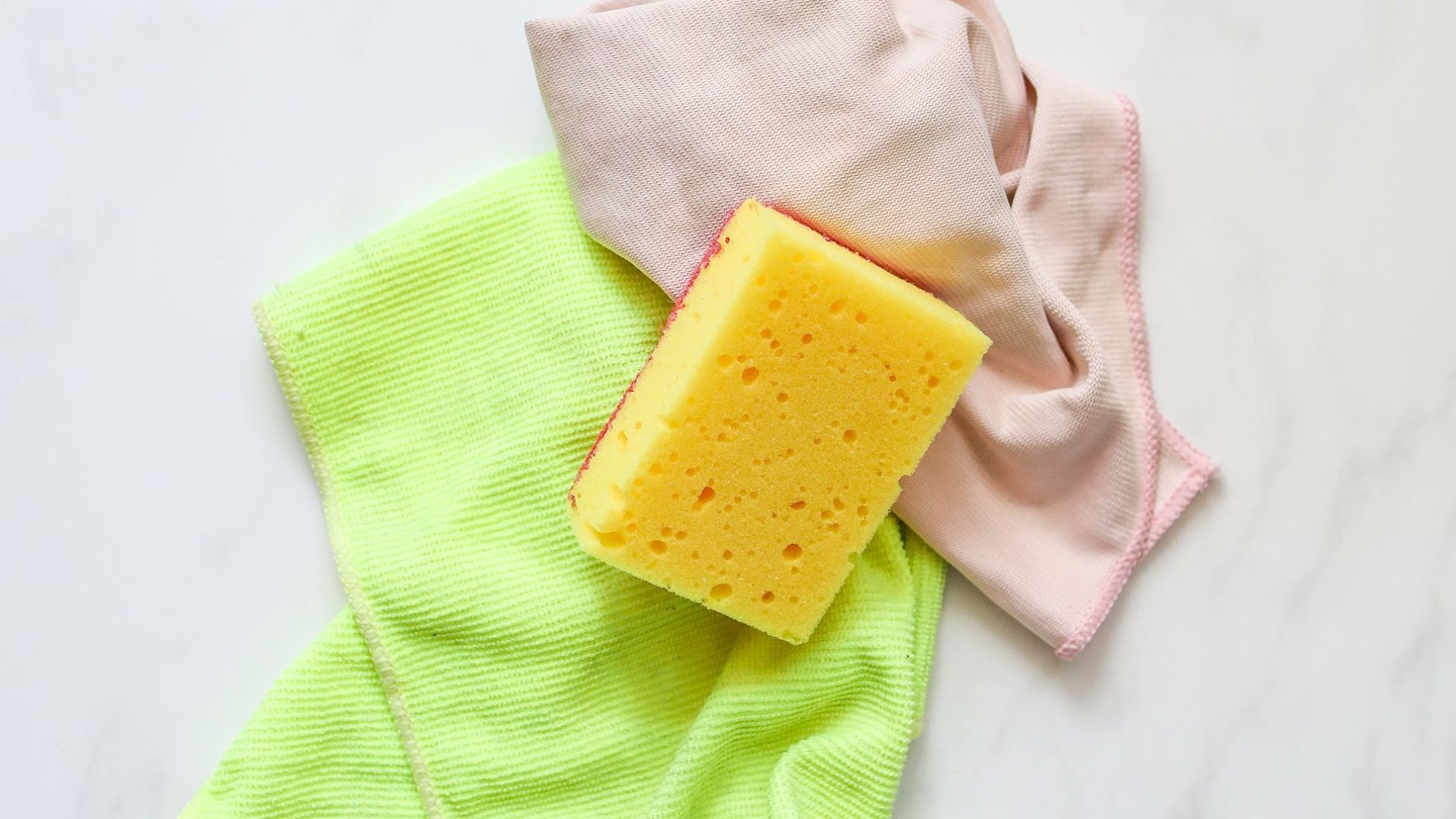 Colorful cleaning supplies with sponge on a marble surface, ideal for housekeeping themes.